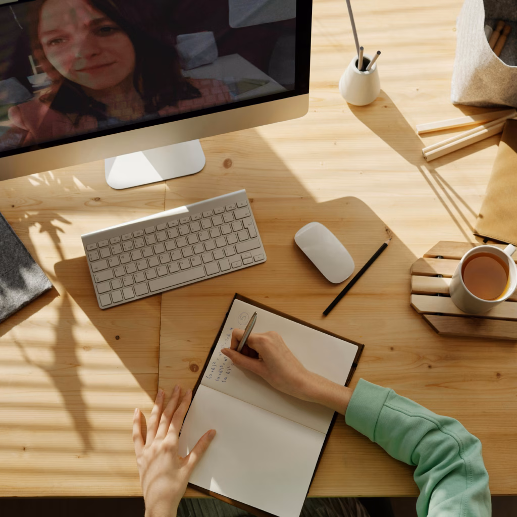 A student taking notes during a video call for online learning at home.