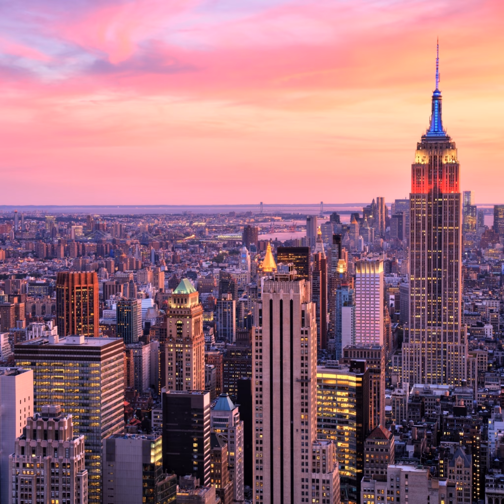 A vibrant sunset over the New York City skyline featuring the Empire State Building and Manhattan’s skyscrapers glowing in pink and orange hues.