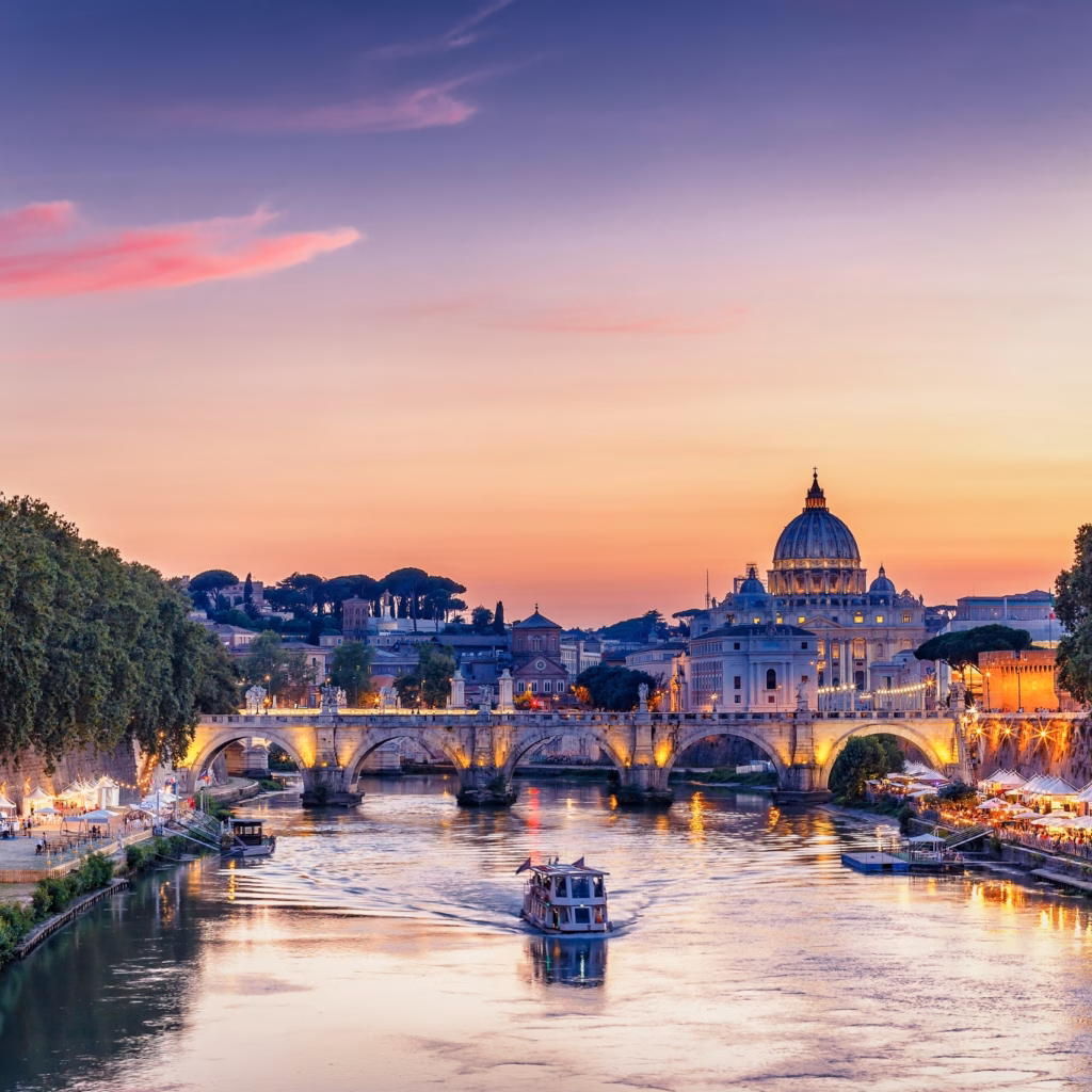 Scenic view of the Tiber River and St. Peter’s Basilica in Vatican City at sunset, with boats on the water and a golden sky illuminating Rome’s architecture.